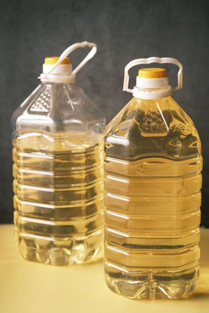 Products Two large recyclable plastic bottles filled with cooking oil on a yellow surface.