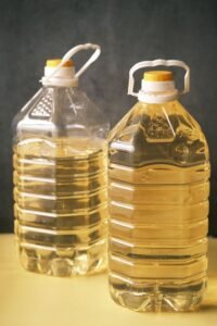 Two large recyclable plastic bottles filled with cooking oil on a yellow surface.