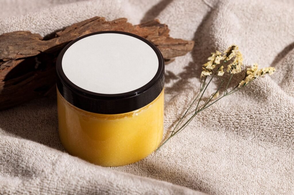 Products Jar of yellow skincare cream on a towel with wood and dried flowers, ideal for spa themes.