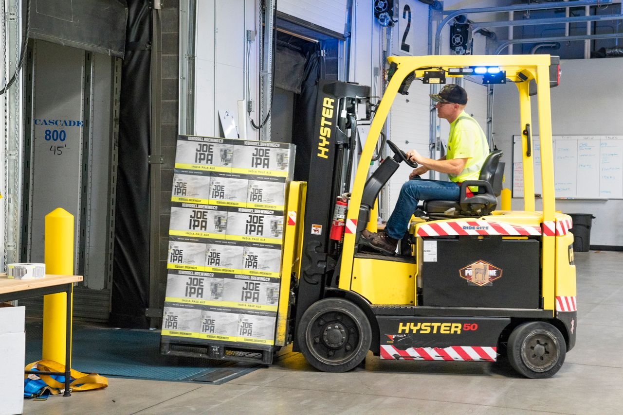 Products A worker drives a Hyster forklift moving Joe IPA boxes in a warehouse.