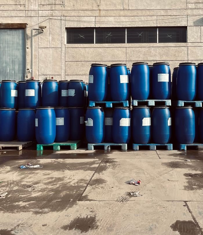 Palm-Derived Industrial Products Rows of blue industrial barrels stacked on pallets outside a warehouse.