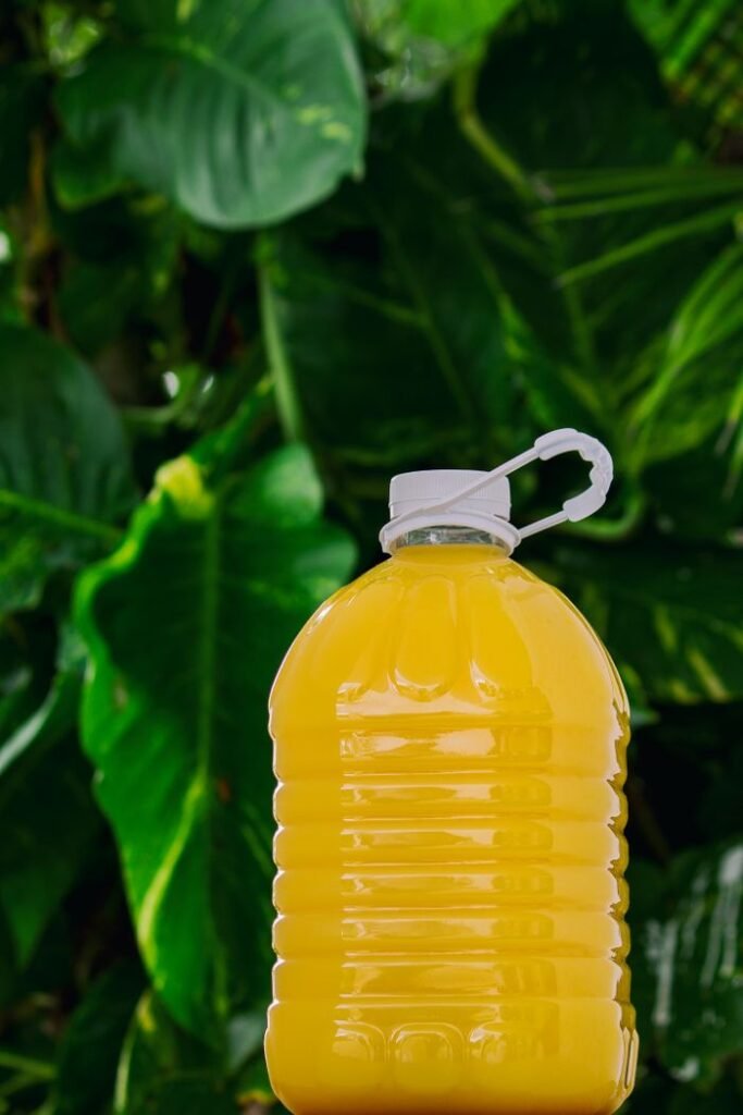 Products A vibrant yellow juice bottle set against lush green tropical leaves, ideal for beverage themes.