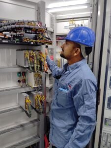 project-2 Electrician in blue helmet checking control panel wiring for safety compliance.