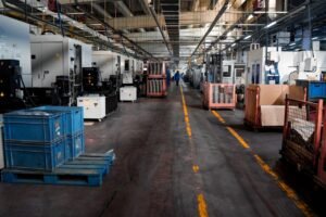 project-3 Vast industrial factory floor with machinery, crates, and structured workstations.