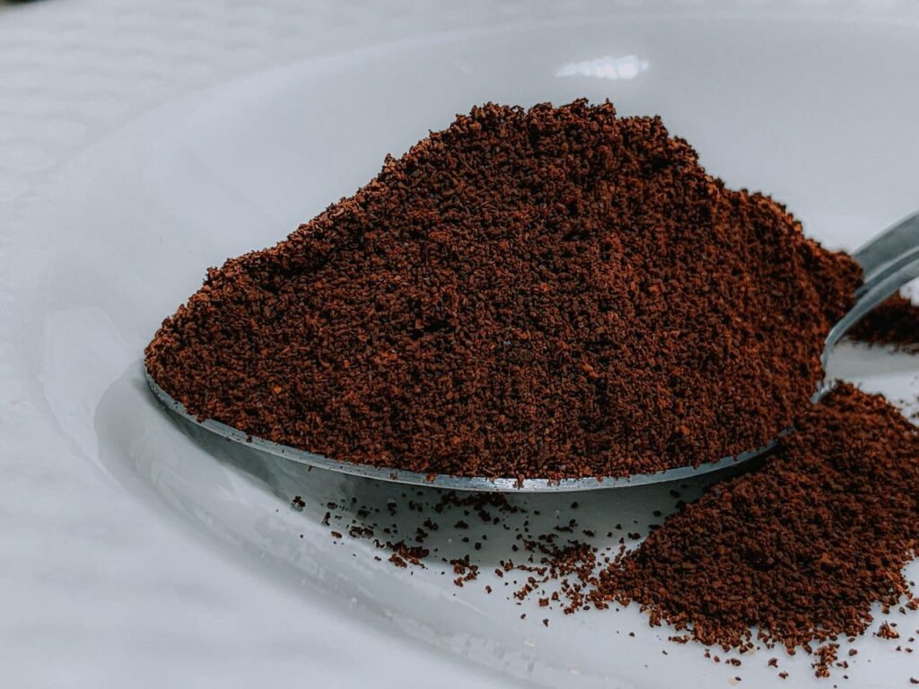 Products Closeup aromatic organic ground coffee heaped in silver teaspoon on white ceramic plate on table in cafeteria kitchen