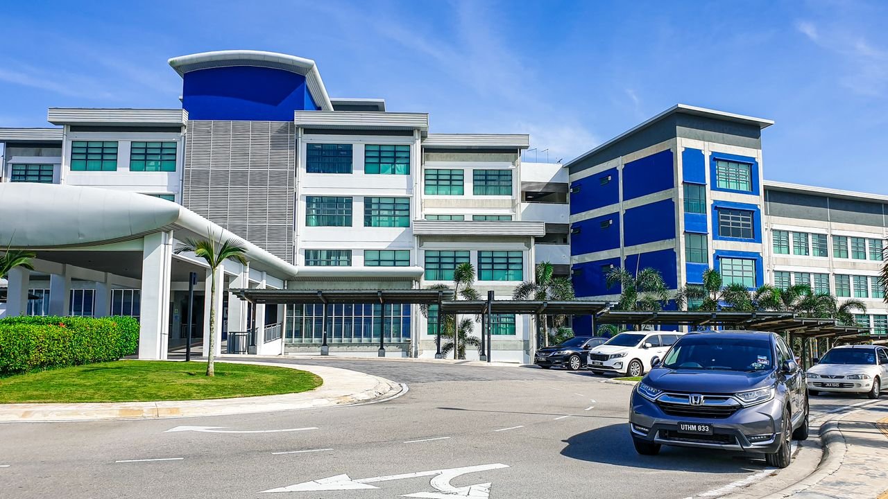 Privacy Policy Modern building with blue accents and parked cars in Johor, Malaysia, under a clear sky.