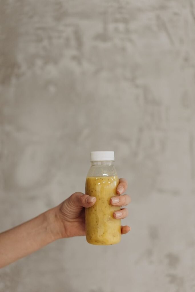Products A hand holding a healthy juice bottle with a neutral background, emphasizing health and lifestyle.