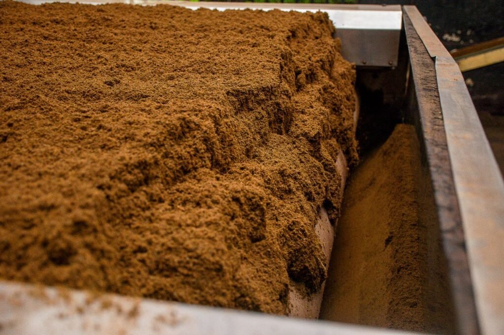 Palm Kernel Products Detailed view of brown soil on an industrial conveyor belt inside a processing facility.