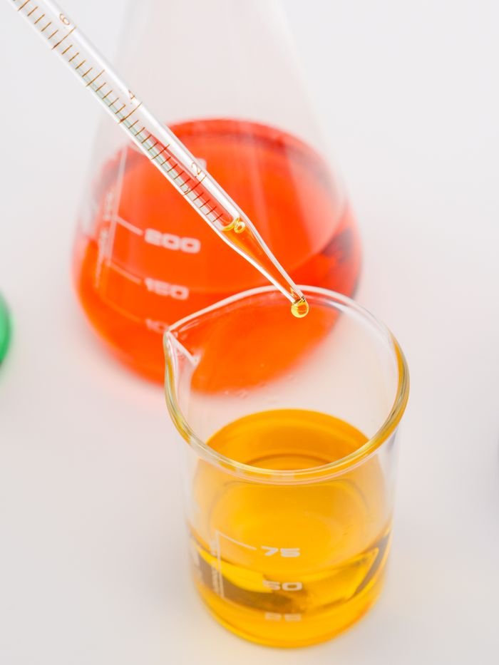 Products Pipette transferring orange liquid into a beaker in a lab setting.