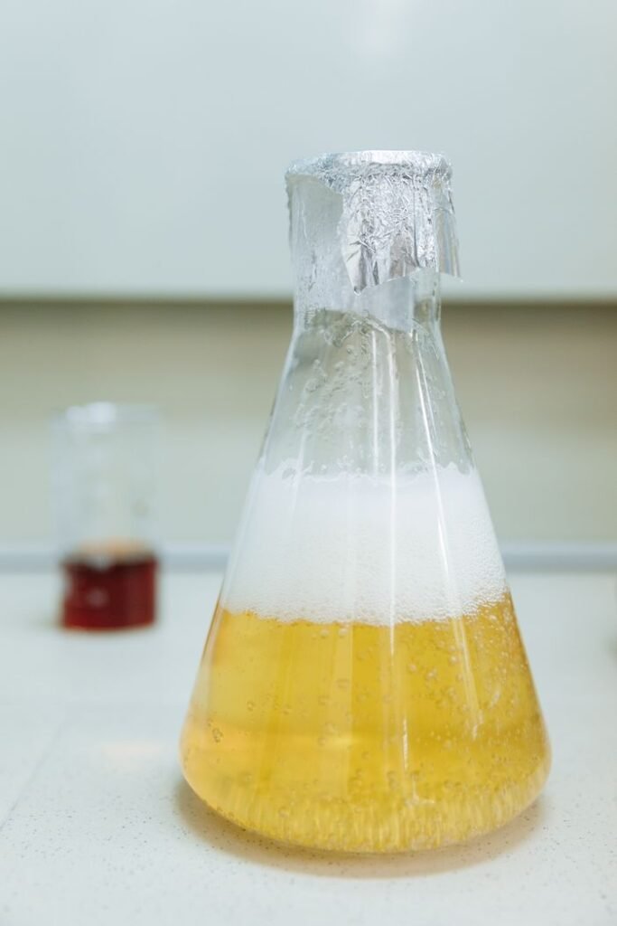 Palm-Derived Industrial Products Close-up of a bubbling liquid in an Erlenmeyer flask wrapped with foil, indoors in a lab.