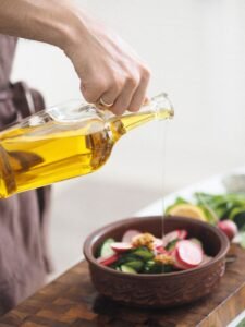 automotive Hand pouring olive oil over a fresh vegetable salad in a kitchen setting.